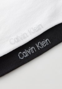 Calvin Klein bomuldsstrømper i hvid og sort. Den hvide strømpe har et lysegråt prægede logo; den sorte strømpe har en kontrasterende hvid logostik.