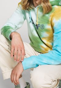 Sudadera con capucha en tie-dye, con colores verde, aqua y amarillo. Cuerdas ajustables y un logo en el pecho. Tejido suave.