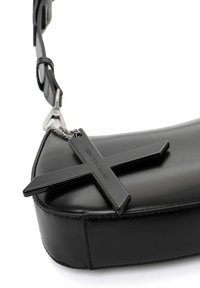 Borsa in pelle nera con una texture liscia, dotata di un prominente charm a forma di croce nera attaccato. La borsa ha una forma elegante e arrotondata e un design minimalista.
