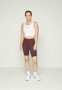 Vit croppad linne med svart logotyp, kombinerad med bordeauxfärgade cykelbyxor med vita sidostrick. Avslutad med vita sportskor.