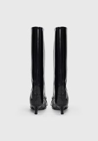 Botas negras hasta la rodilla con un acabado brillante, punteras puntiagudas y tacones finos. Detalle de cremalleras laterales y material de textura suave.