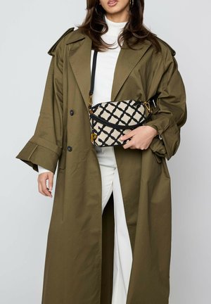 Green trench coat with wide sleeves, paired with a patterned crossbody bag featuring a black geometric design on a cream background.