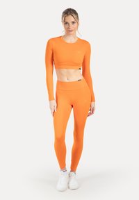 Helder oranje crop top met lange mouwen en bijpassende hoge taille legging, gemaakt van glad, rekbaar materiaal, met een subtiel merklogo.