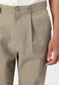 Naborane khaki hlače od teksturiranog materijala, sa zatvaranjem na dugme i bočnim džepovima, s mekim, naboranim izgledom.