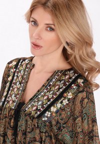 Bluză brodată cu un model floral și paisley. Țesătură închisă la culoare cu accente colorate în jurul gâtului și o croială lejeră.