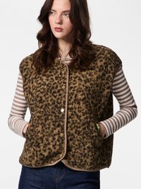 Woman with wavy brown hair wearing a brown leopard print textured vest over a beige and white striped long-sleeve shirt and blue jeans.