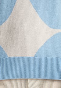 Light blue sweater featuring large white abstract shapes, with ribbed cuffs and hem. The texture appears soft and knit.