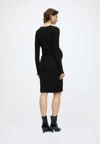 Μαύρο ριμπ φόρεμα με μακριά μανίκια, εφαρμοστή σιλουέτα, μήκος μέχρι το γόνατο, συνδυασμένο με γυαλιστερά μαύρα μποτάκια αστραγάλου και ομαλή υφή.