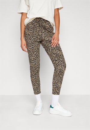 Leopardprint leggings in bruin en zwart, gemaakt van rekbare stof en met een elastische tailleband. Gecombineerd met witte sneakers en witte sokken.