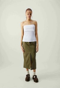 Biela top bez ramienok s priliehajúcim korzetom, skombinovaná s olivovozelenou midi sukňou s vysokým pásom a predným rozparkem. Hnedé platformové topánky.