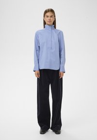 Chemise bleu clair à col avec patte de boutonnage, manches longues et coupe décontractée, associée à un pantalon ample bleu marine en velours côtelé.