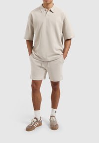 Beige poloshirt met korte mouwen, met een klein logo. Gepaard met bijpassende beige shorts en bruine sneakers, inclusief witte sokken.
