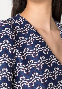 Tkanina w kolorze granatowym z wzorem w zygzaki w białym i burgundowym, o teksturowanej powierzchni i dekolcie w serek.