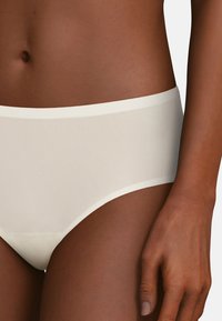 Witte naadloze hipsteronderbroek met een gladde textuur en een brede tailleband, van opzij weergegeven tegen een neutrale achtergrond.