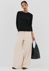 Maglione nero a maniche lunghe, pantaloni larghi color crema e borsa nera con dettagli metallici. Tessuto morbido e vestibilità casual.