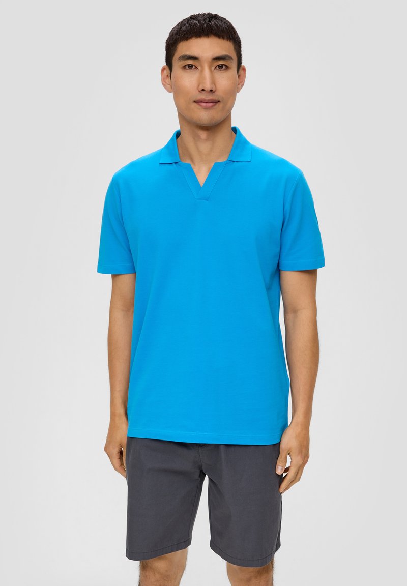 Türkise Poloshirt mit V-Ausschnitt, kurzen Ärmeln und glatter Textur. Kombiniert mit grauen Shorts, vor einem neutralen Hintergrund präsentiert.