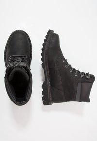Botas de cuero negras con suela robusta, diseño de cordones y acentos texturizados. Cuentan con cuello acolchado y detalles de costura reforzados.