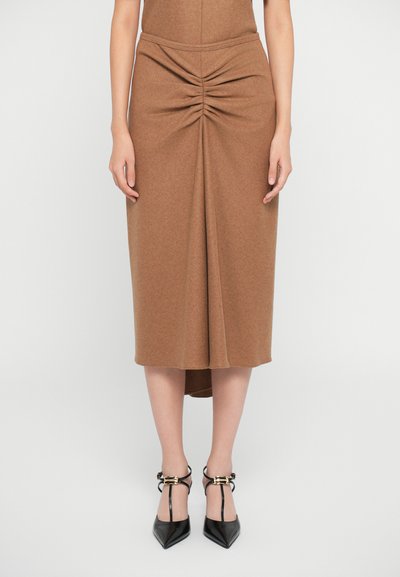 Bruine midi-rok met geplooide details bij de taille, gemaakt van zachte stof. Gecombineerd met zwarte puntige hakken met enkelbandjes.