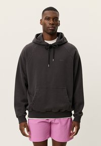 Μαύρο φούτερ με κουκούλα, τσέπη καγκουρό, κορδόνι και ριμπ τελείωμα. Φοράει ροζ κοντό σορτς με υφή από κάτω.