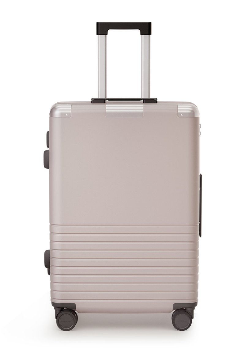 Harde koffer in metallic roségoud, met een telescopische handgreep, getextureerde horizontale ribbels en vier wielen voor mobiliteit.