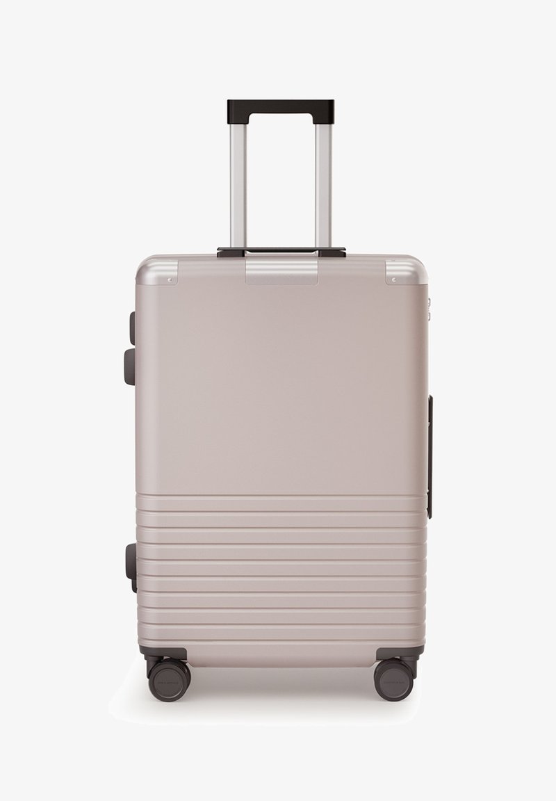 Harde koffer in metallic roségoud, met een telescopische handgreep, getextureerde horizontale ribbels en vier wielen voor mobiliteit.