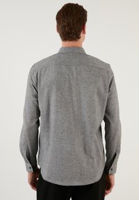Grå knap-up skjorte lavet af tekstureret stof, vist fra bagsiden med en buet kant og lange ærmer. Har knapper ved ærmerne.