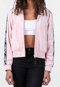 Chaqueta bomber rosa con cremallera frontal, puños y cintura acanalados, con franjas laterales negras y detalles de logo en blanco. Textura de tela suave.