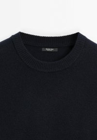 Pull en maille bleu marine foncé avec col rond côtelé et une étiquette indiquant "Massimo Dutti Made in China" à l'intérieur du col.