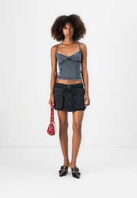 Denimová crop top s tenkými ramínky, má zakřivené švy. Černá denimová sukně, krátká s dvěma předními kapsami. Červená kabelka s vzorem a černé muly na podpatku.