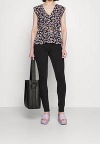 Blouse noire à motifs floraux avec manches courtes, ornée de feuilles roses et violettes. Portée avec un jean noir et des sandales à plateforme lavande. Sac fourre-tout noir.
