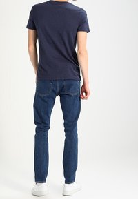 Mörkblå kortärmad t-shirt i kombination med ljusblå slim-fit jeans och vita sneakers, med synlig sömnad på jeansmaterialet och en klassisk design.