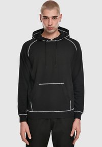 Melns džemperis ar kapuci no mīksta auduma, ar baltām izšuvuma detaļām, priekšēju kabatu, regulējamām auklām un kapuci.