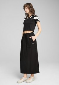 Svart cropped topp med vita accenter, tillsammans med en svart maxikjol med två stora fickor. Modellen bär grå skor.