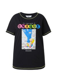 Camiseta negra con un gráfico colorido que dice "TODO LO QUE NECESITAS ES ÚNICO" y una impresión de zapatillas. Mangas cortas con un ribete verde contrastante.