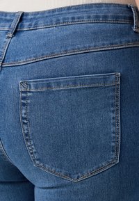 Dark blue denim jeans featuring a back pocket with stitching details and a slight fade. Material is smooth with a medium-weight texture.