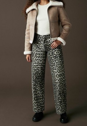 Chaqueta beige con cuello de piel sintética y cremallera, combinada con jeans de pierna ancha de estampado de leopardo y botas negras.