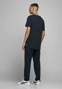 Marineblå tekstureret t-shirt med korte ærmer, parret med mørke bukser og hvide sneakers med et sort mønster. Bagansigt af outfittet.