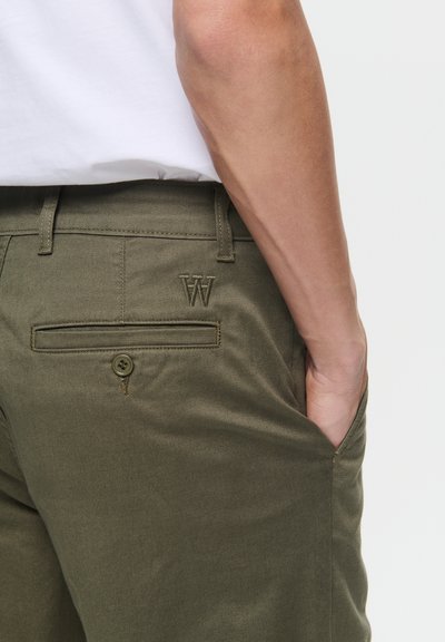 Pantalons vert olive en mélange de coton, avec une poche arrière boutonnée, des passants de ceinture et un logo "W" brodé à l'arrière.