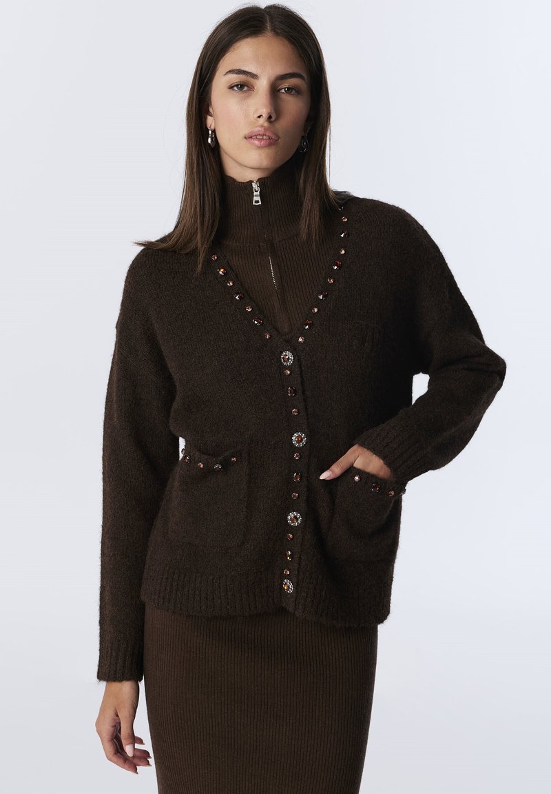 Bruine gebreide cardigan met decoratieve knopen, twee voorkruiden, ribgebreide manchetten en een V-hals ontwerp boven een bijpassende ribgebreide jurk.