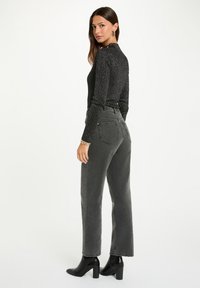 Top lungo a maniche nere a coste abbinato a jeans in denim grigio a vita alta e stivaletti neri. Caratterizzato da un design aderente e una gamba dritta.