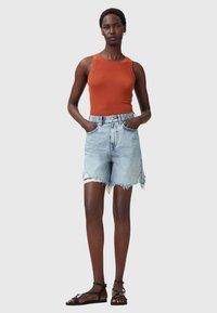 Oranje tanktop en lichtblauwe denimshorts met rafelrand, voorzien van frontzakken. Zwarte platte sandalen met verstelbare banden.