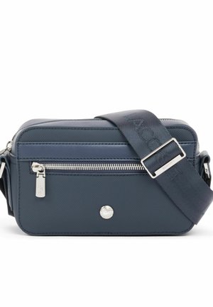 Bolso bandolera rectangular azul marino con cremallera plateada, logotipo metálico redondo y correa ancha de tela ajustable con nombre de la marca en relieve.