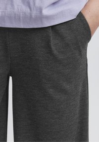 Tmavě šedé, měkké kalhoty ze soft tkaniny s uvolněným střihem, které mají boční kapsy a jemnou strukturu. Žádné viditelné vzory ani kovové detaily.