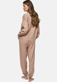 Ensemble de vêtements de loisirs en tricot beige comprenant un pull à coupe décontractée et un pantalon à cordon de serrage, avec des poignets et un ourlet côtelés, une texture douce et un design minimal.
