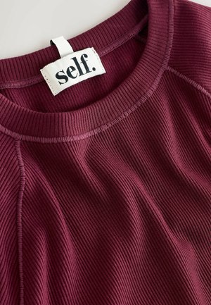 Bordo spalvota megztinis su apvaliu kaklu, su etikete "self." ir tekstūrine medžiaga, suteikiančia papildomą dimensiją.