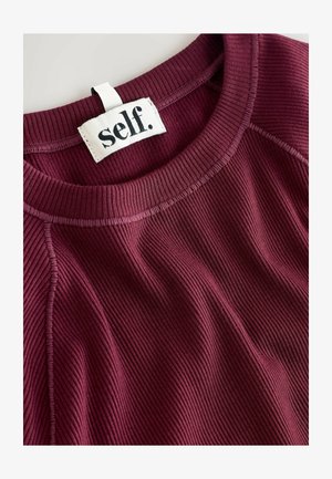 Burgunderfarbener gerippter Pullover mit rundem Ausschnitt, der ein Etikett mit der Aufschrift "self." und ein strukturiertes Material für zusätzliche Dimension aufweist.