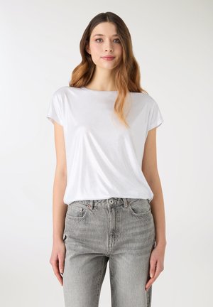 Biały t-shirt z krótkim rękawem wykonany z lekkiego, gładkiego materiału. Połączony z jasnoszarymi, wysokim stanem i prostymi nogawkami jeansami.