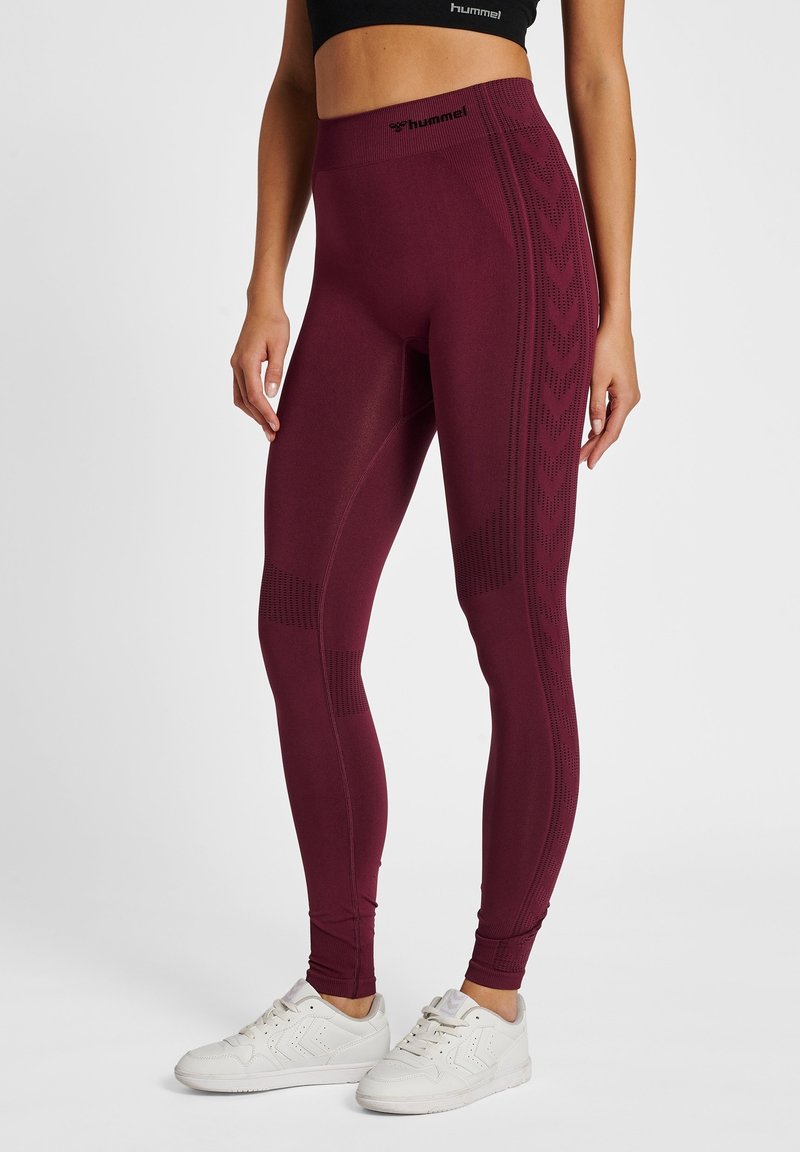 Leggings burdeos de talle alto hechos de material elástico, con patrones texturizados en los laterales y un logo en la cintura.