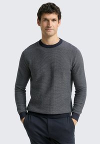 Pullover aus Strick in Marineblau mit strukturiertem Muster und Rundhalsausschnitt. Enganliegende Bündchen und Saum, kombiniert mit dunkler Hose.