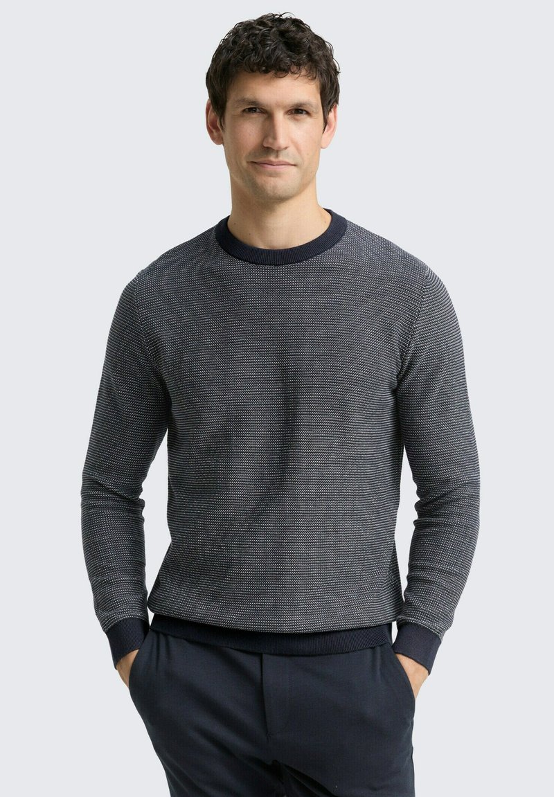 Pullover aus Strick in Marineblau mit strukturiertem Muster und Rundhalsausschnitt. Enganliegende Bündchen und Saum, kombiniert mit dunkler Hose.